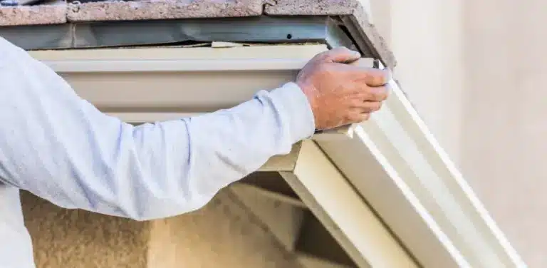 Contractor's hand cleaning debris from residential gutter and downspout during maintenance work.