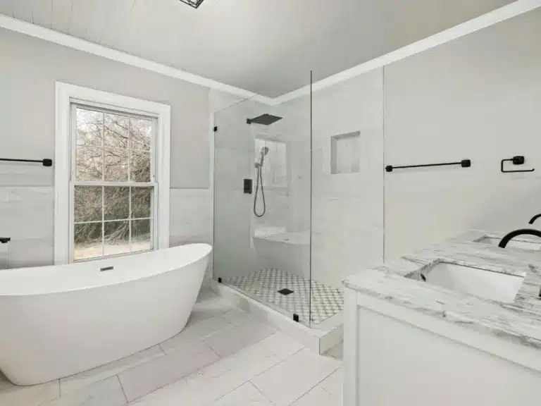 Modern bathroom with white marble countertops, freestanding tub, walk-in shower with glass enclosure, and large window.