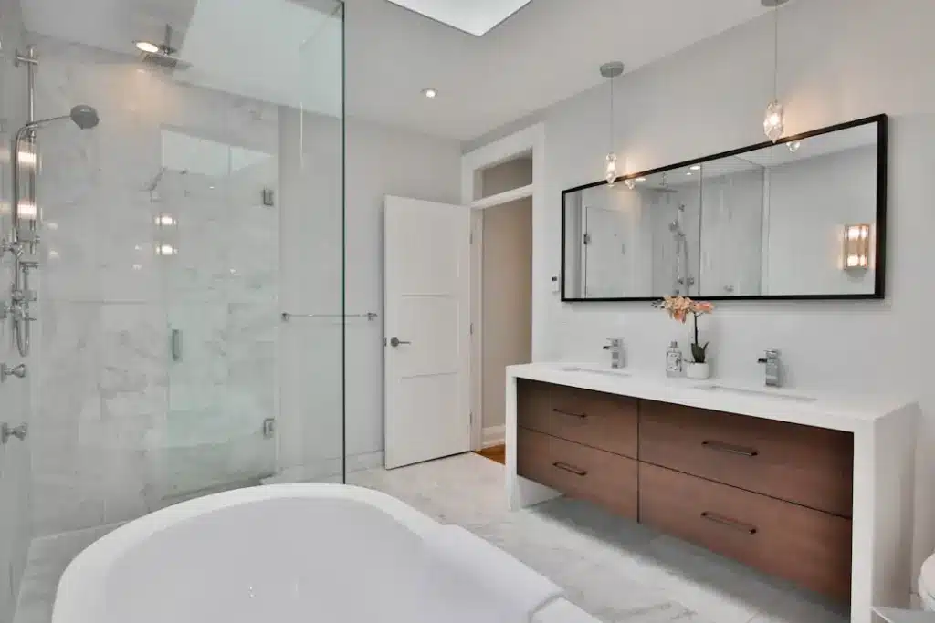 Modern bathroom with freestanding tub, marble shower enclosure, wood vanity, and pendant lighting.