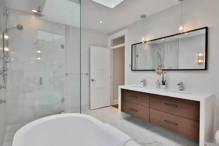 Modern bathroom with freestanding tub, marble shower enclosure, wood vanity, and pendant lighting.