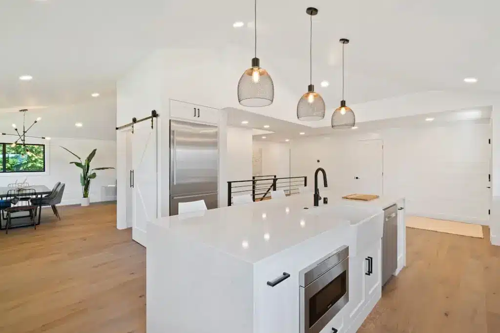 Modern kitchen with white island, stainless steel appliances, pendant lights, and hardwood floors.
