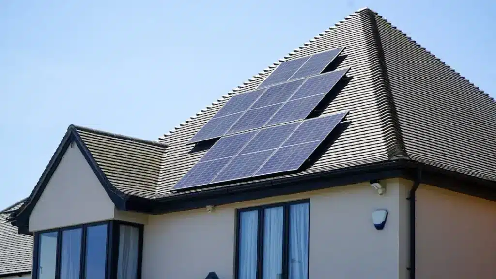 Solar panel array installed on residential roof with dark shingles and white exterior walls.